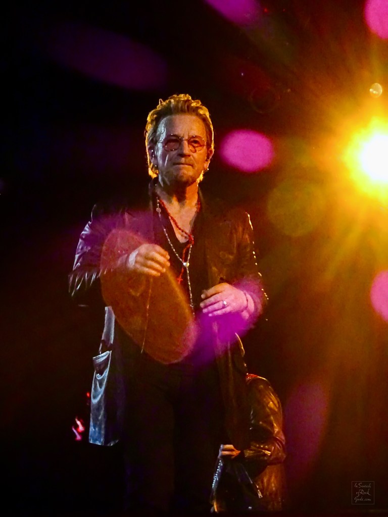A photo of Bono with a burst of yellow light and pink light spots on the right side of the photo. From the U2:UV Achtung Baby at the Sphere concert in Las Vegas March 1, 2024. 