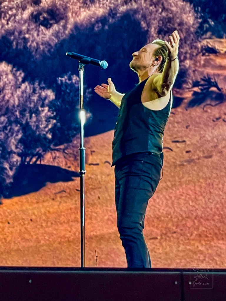 A photo of Bono standing in front of the microphone stand in profile with his arms wide open from the U2:UV Achtung Baby at the Sphere concert in Las Vegas March 1, 2024. 