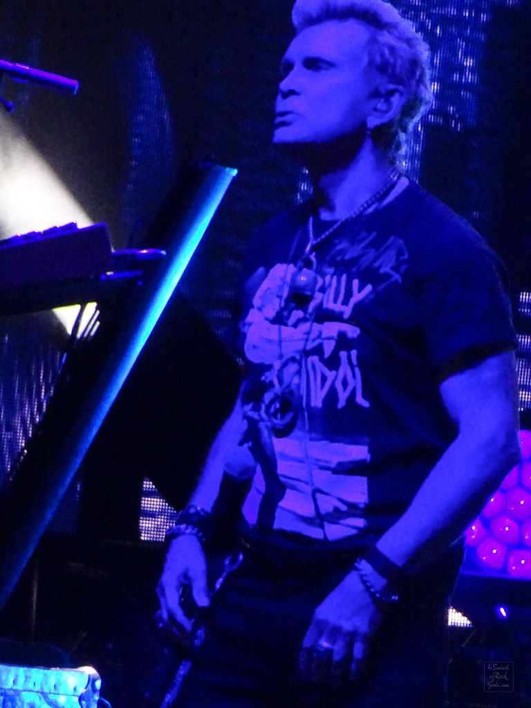 A 3/4 profile photo of Billy Idol in blue light in concert at Rogers Place Edmonton Aug 1 2024.