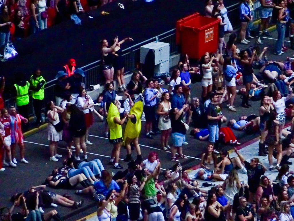 The audience - two  people dressed as bananas dancing and others laying on the ground during Coming Up Roses Harry Styles Together Together Wembley N3 June 17 2026